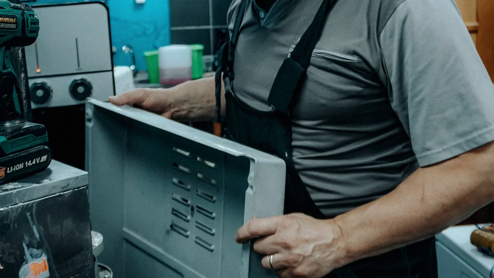 A repair technician lifting the back panel off a household appliance on a workbench.