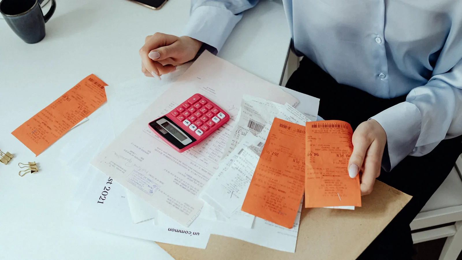 A person sorting receipts beside a calculator at a desk.