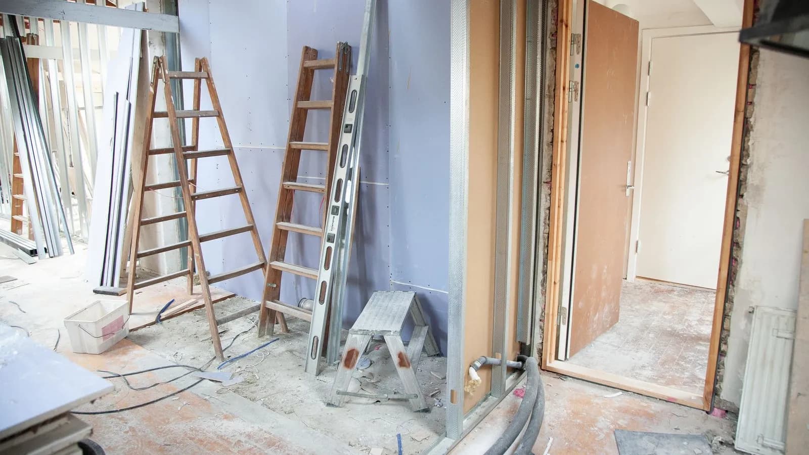 A room mid-renovation with stepladders, metal wall framing and an open doorway.