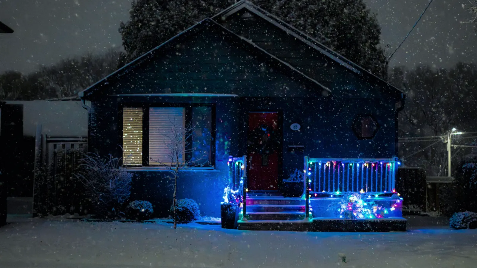 A small house strung with colourful Christmas lights on a snowy night.
