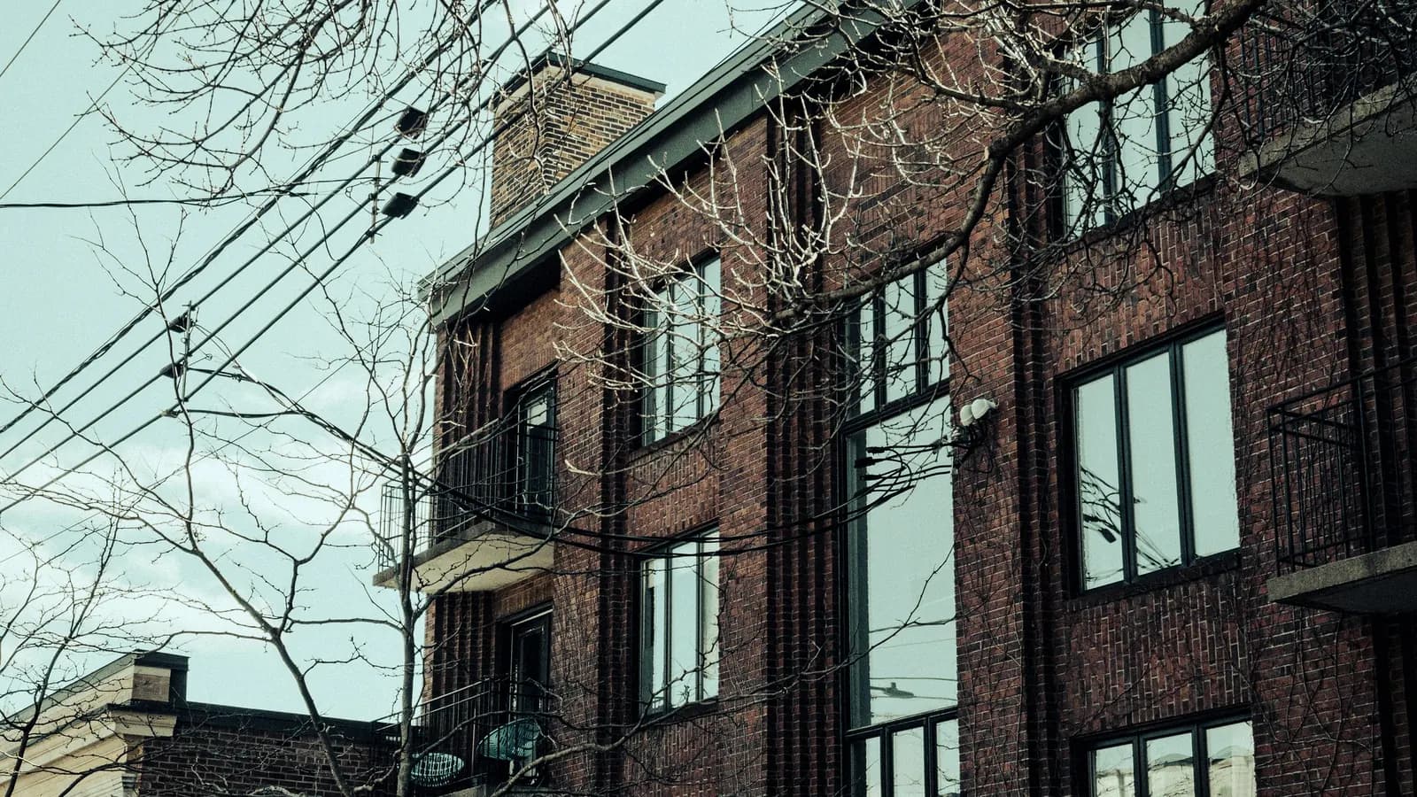 A three-storey red brick apartment building with balconies, seen from the street.