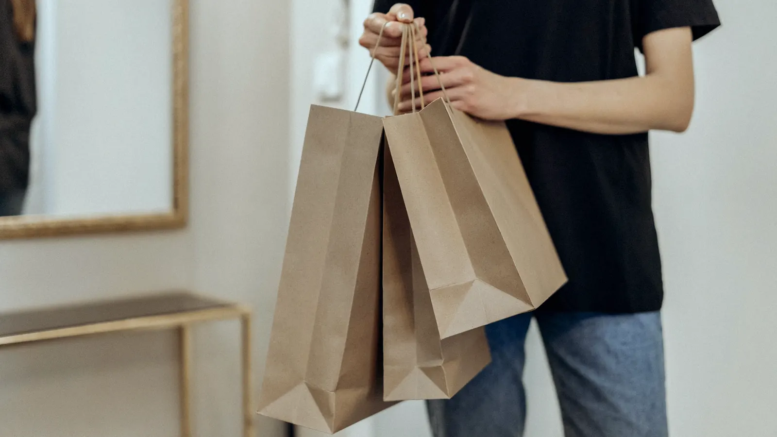 A person holding three brown paper shopping bags.