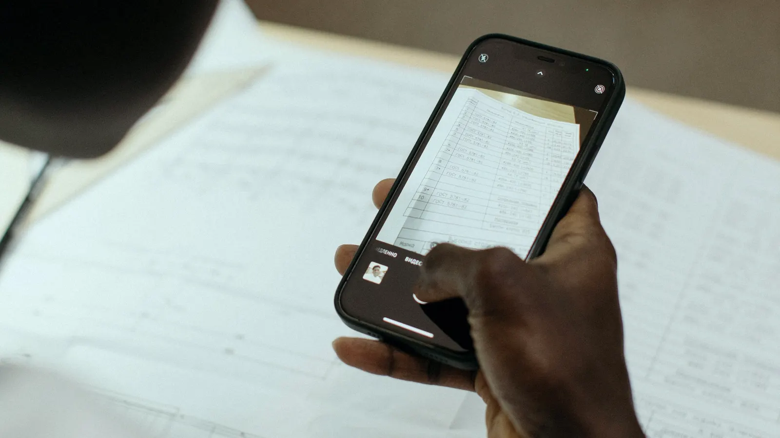 A hand holding a smartphone over a printed document, capturing it with the camera.
