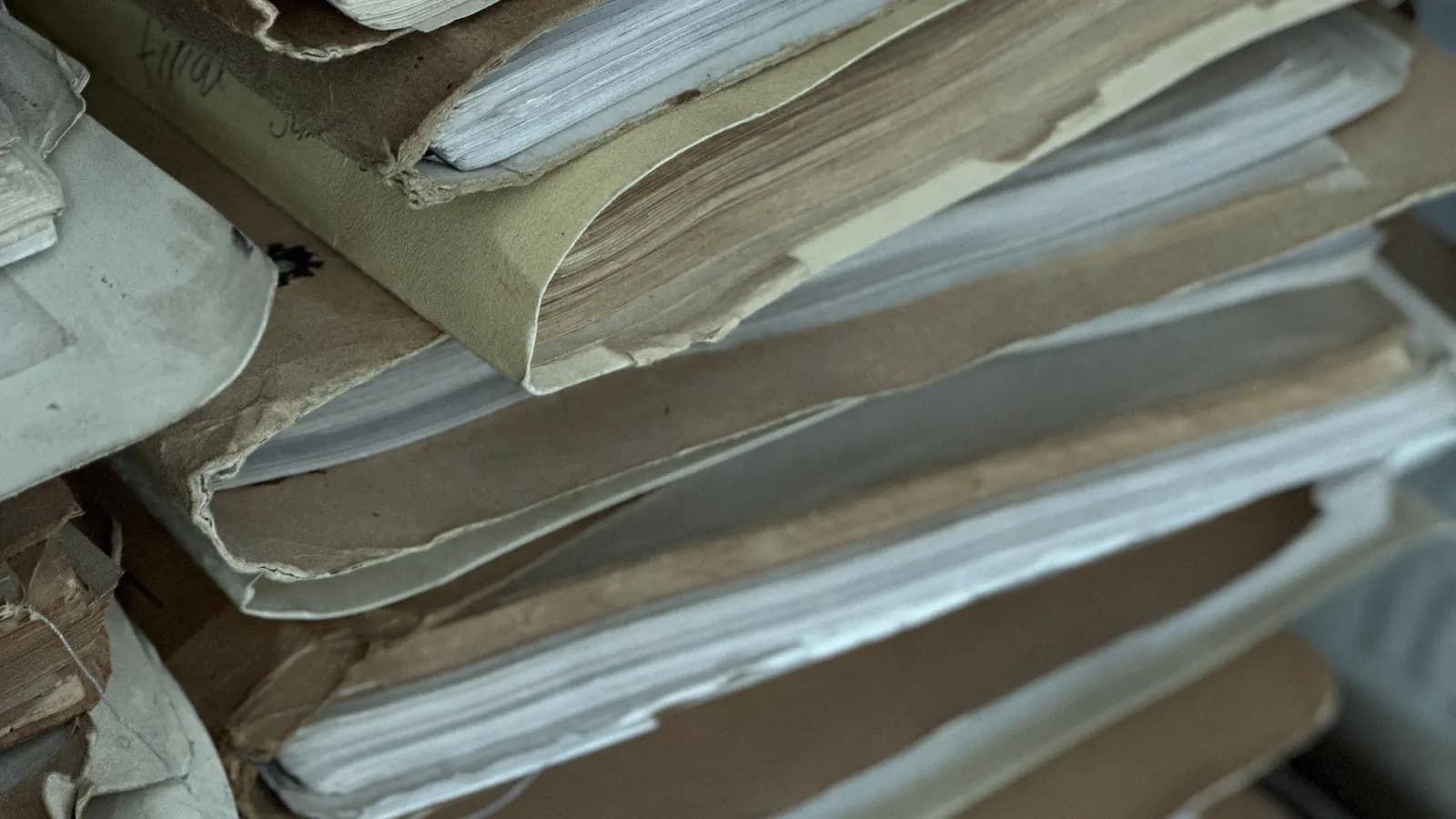 Stacks of old paper files and folders, bulging with documents.