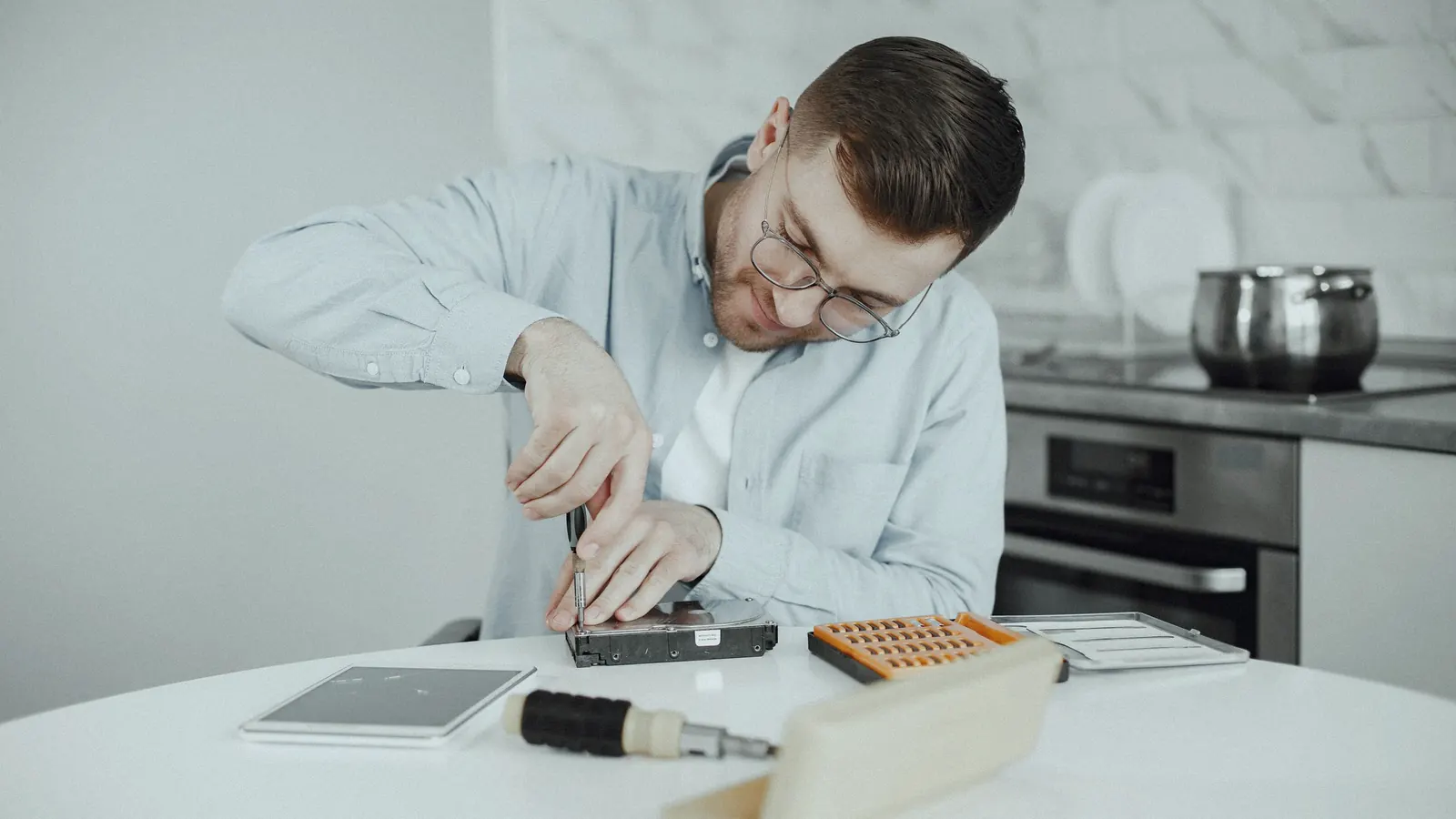 A man with a screwdriver repairing a small device at a kitchen table.