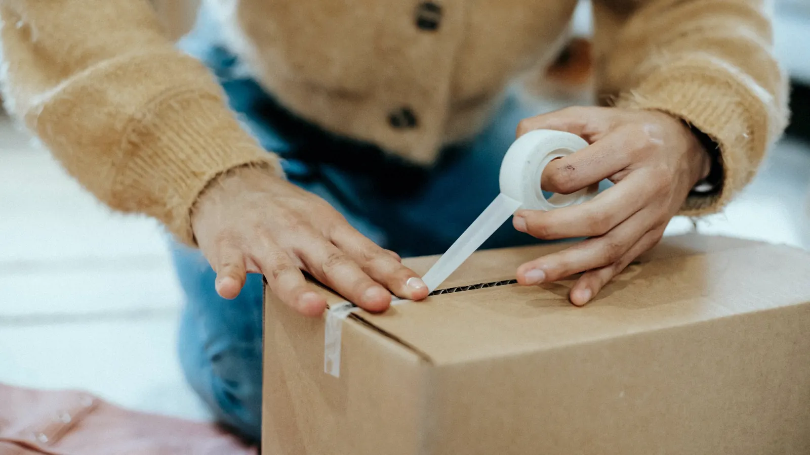 A person sealing a cardboard box with packing tape.
