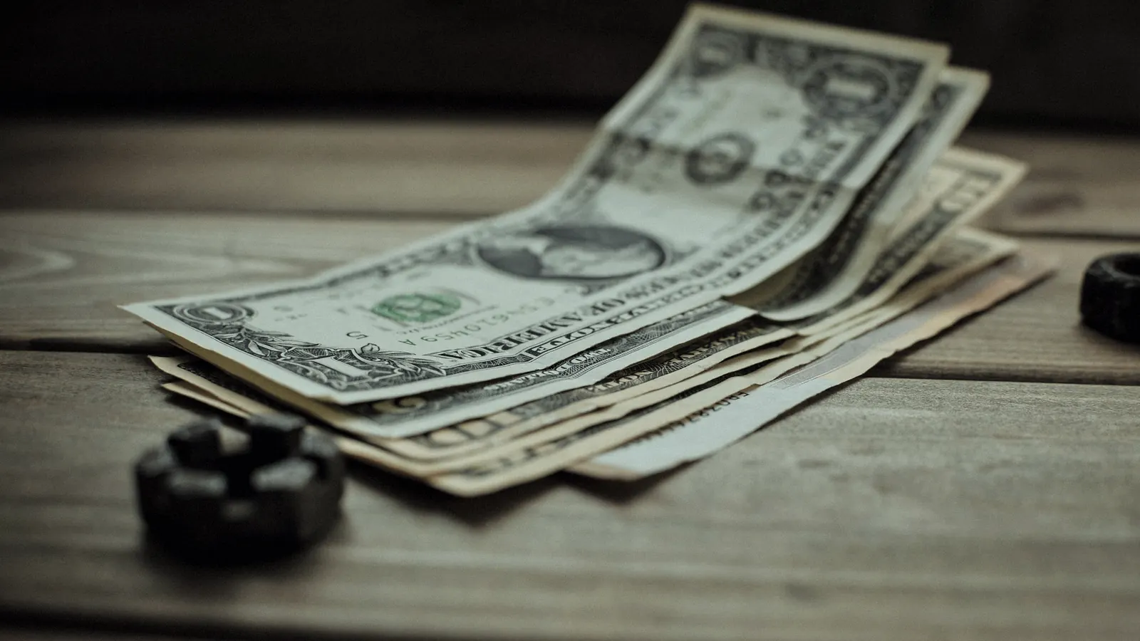US dollar bills fanned out on a wooden table.