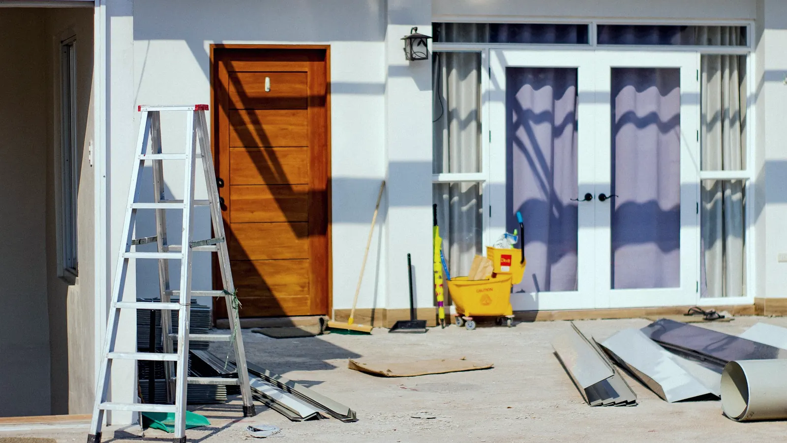The front of a house mid-renovation, with a ladder, tools and building materials outside.