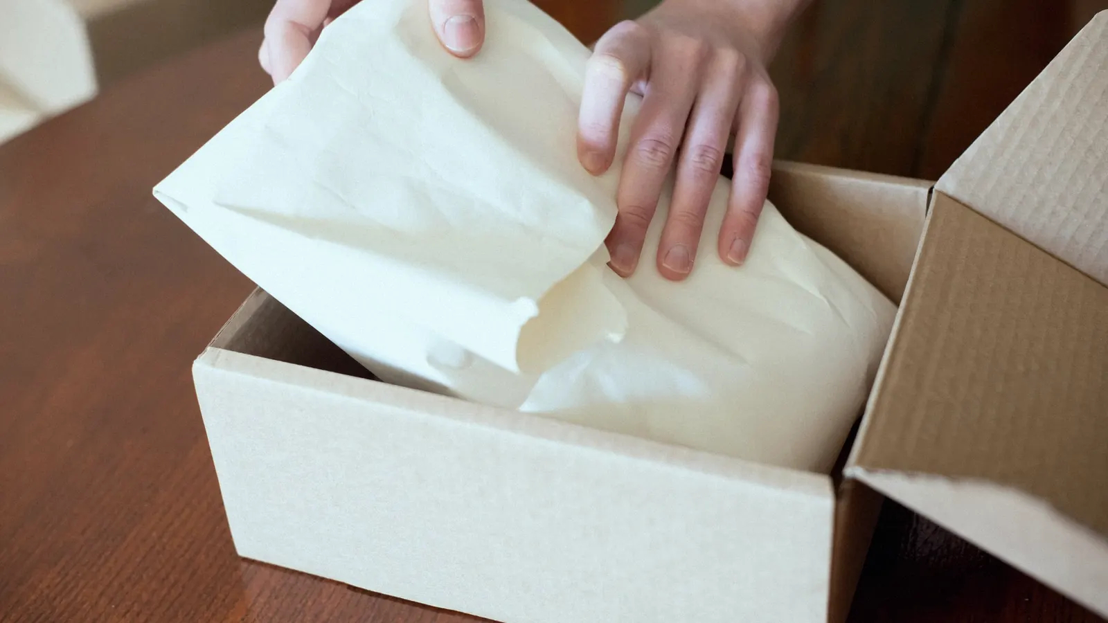 Hands packing an online order into a cardboard box.