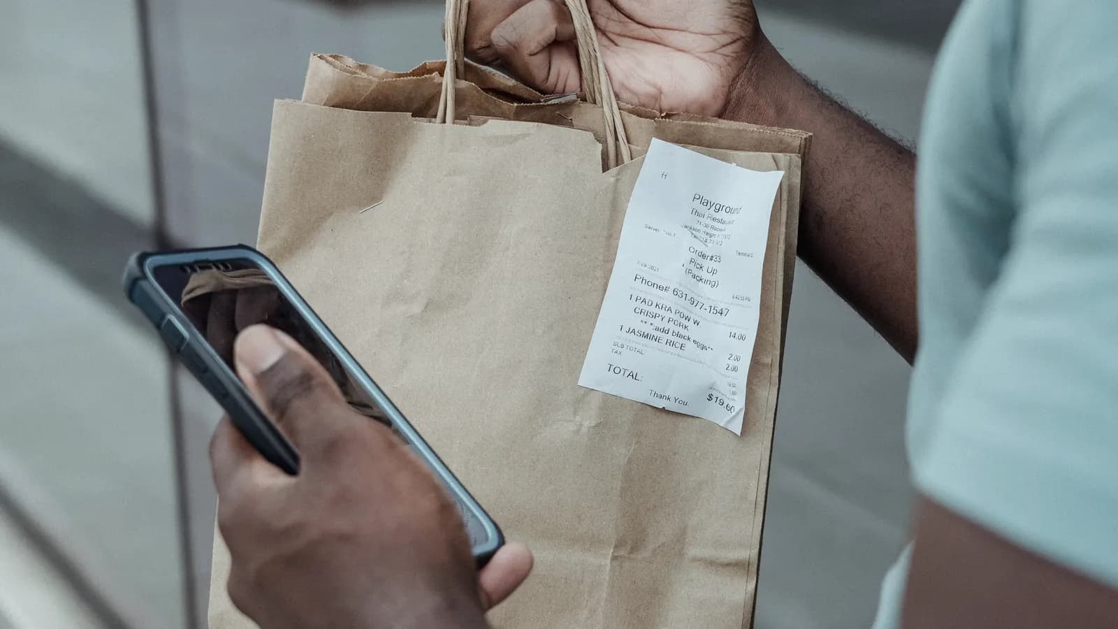 A shopper holding a paper bag with a receipt clipped to it while using a phone.