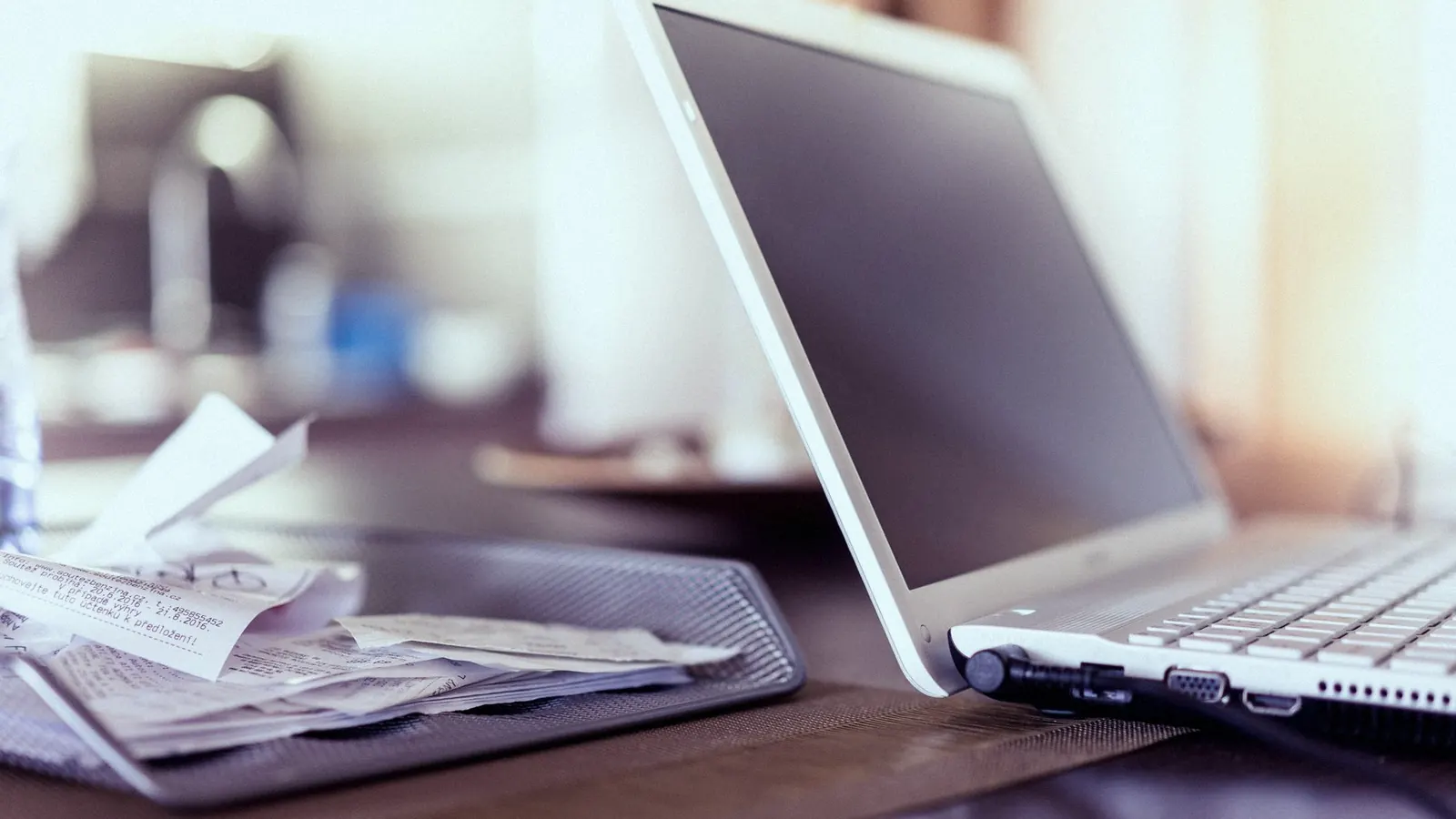 A tray of crumpled paper receipts stacked beside an open laptop on a desk.