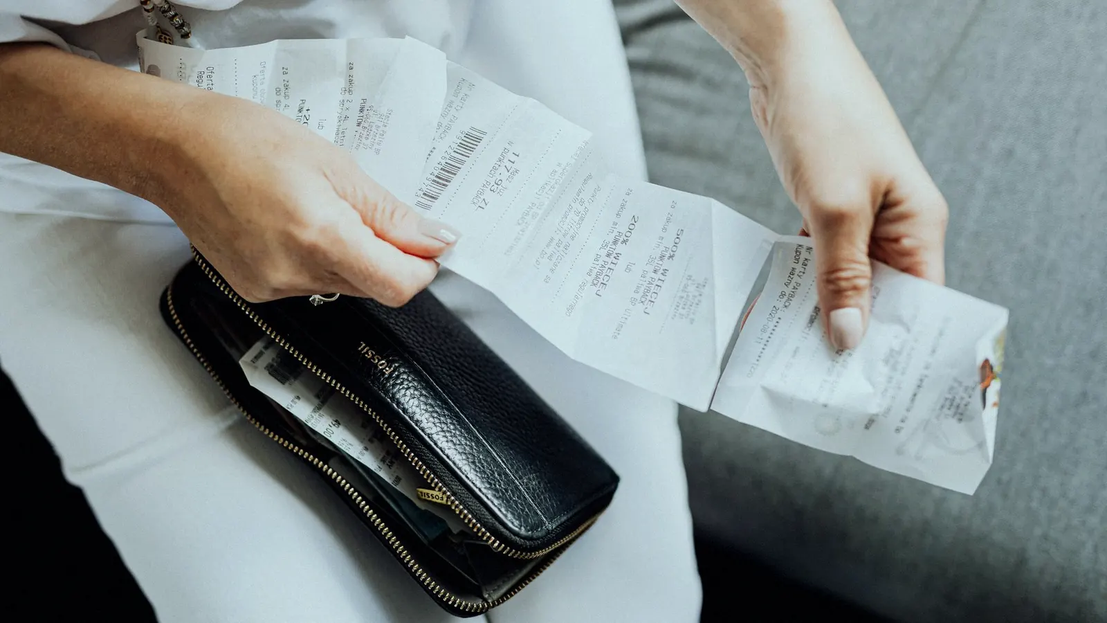 A shopper pulling a handful of folded paper receipts out of a leather wallet.