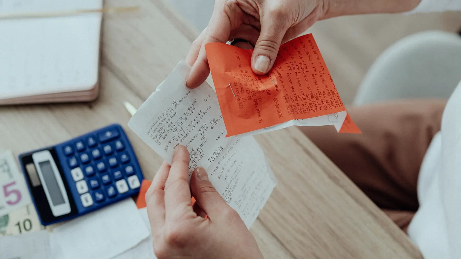 Hands sorting a spread of paper receipts across a desk beside a calculator and a laptop.