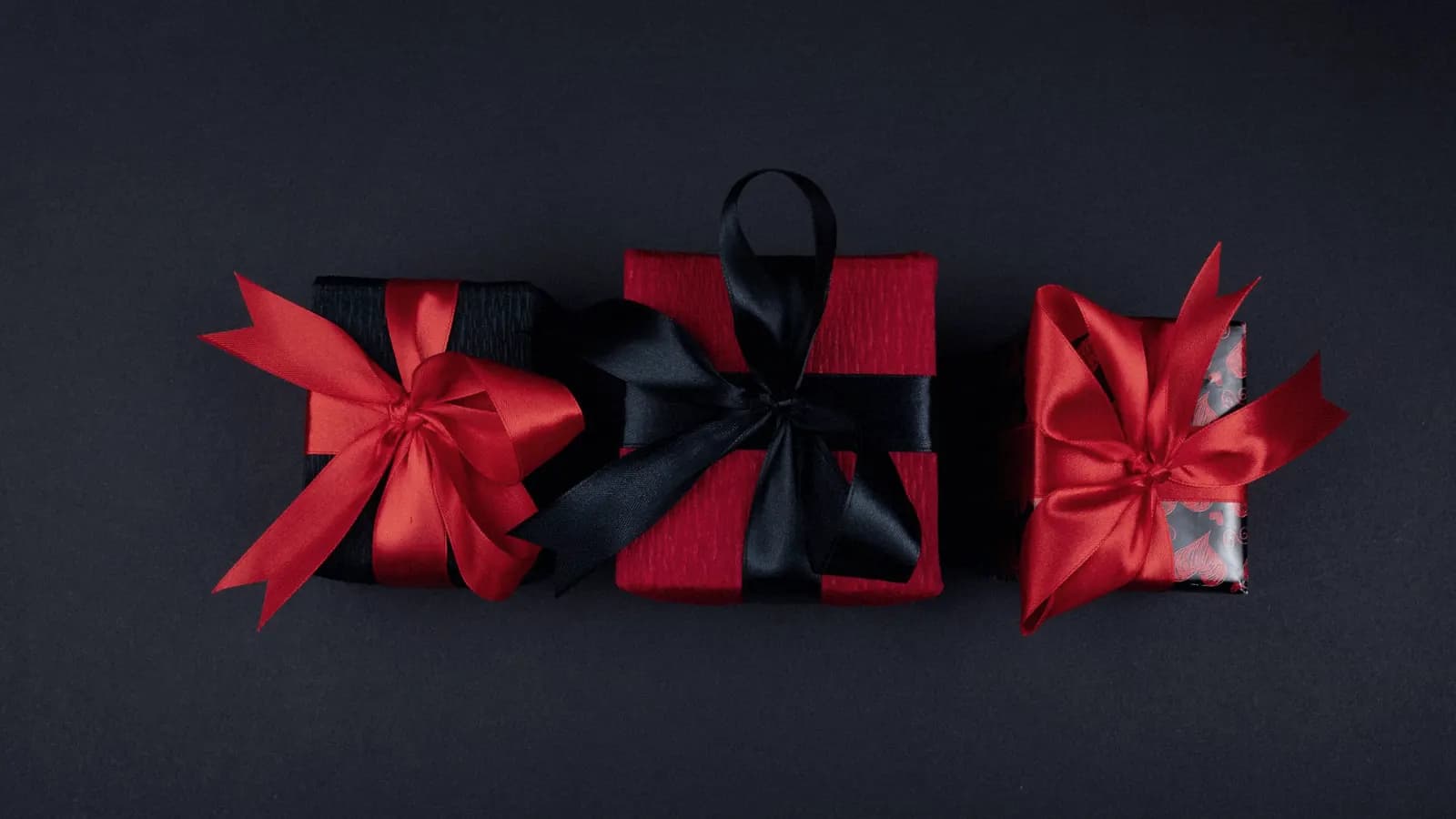 Three presents wrapped in red and black ribbon on a dark background.