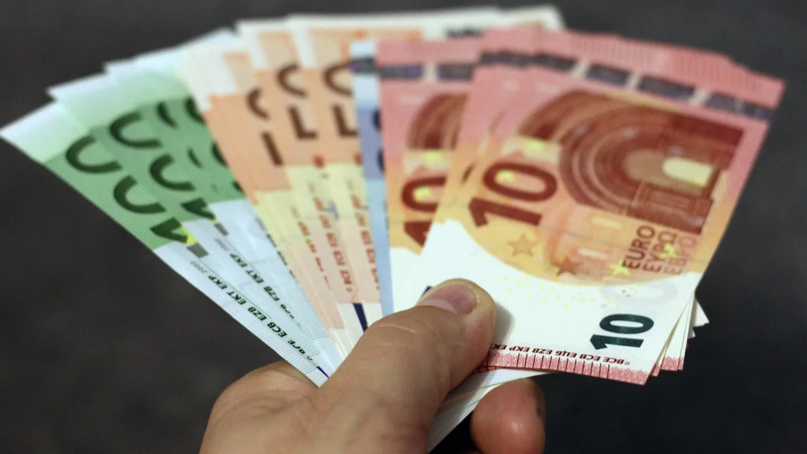 A hand holding a fan of euro banknotes.