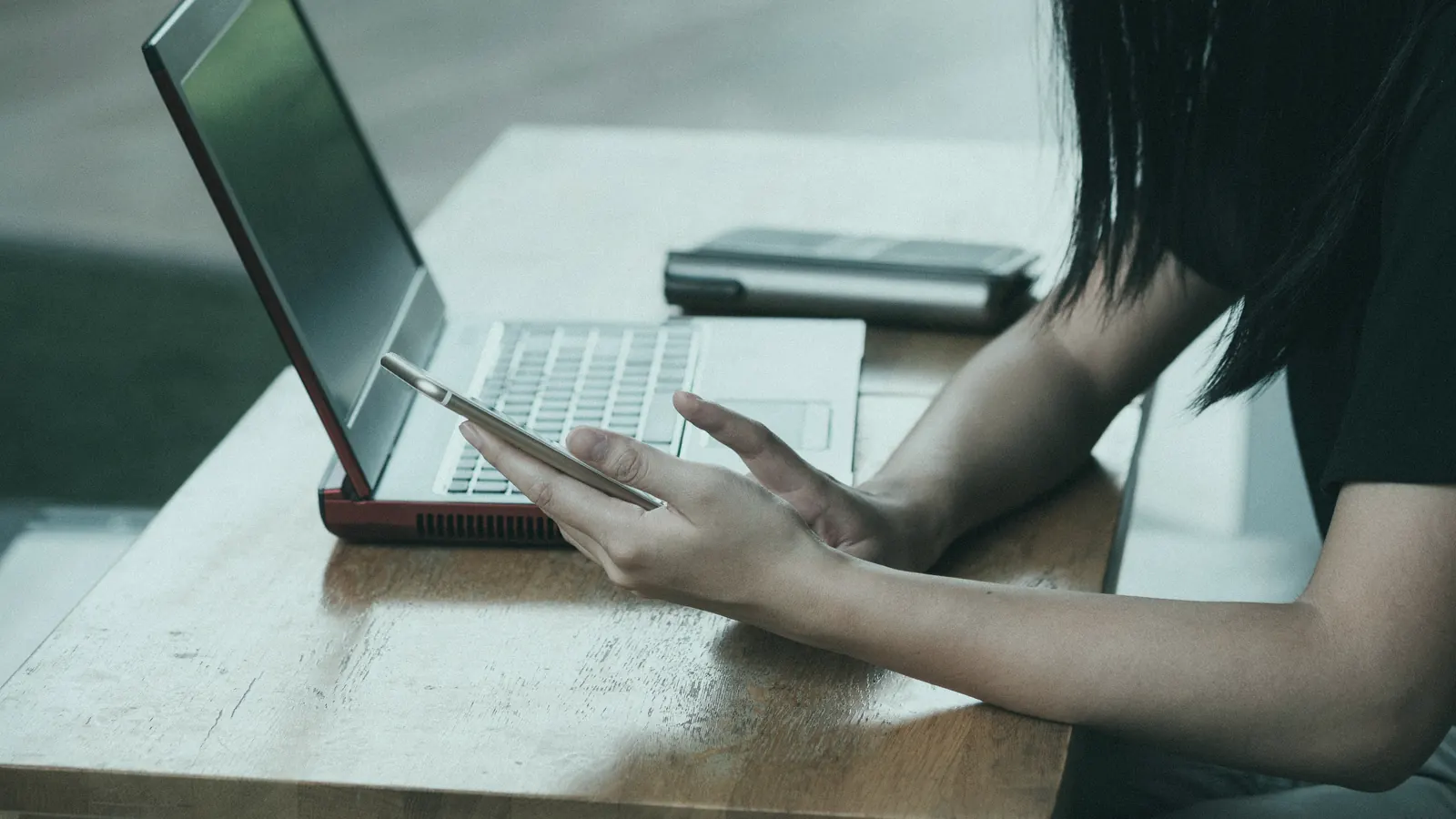 A person at a desk holding a phone beside an open laptop.