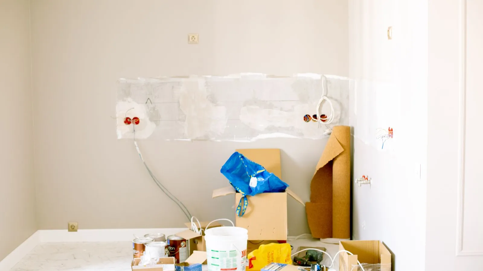 A room being renovated, with exposed wiring on the wall and paint cans, boxes and supplies on the floor.