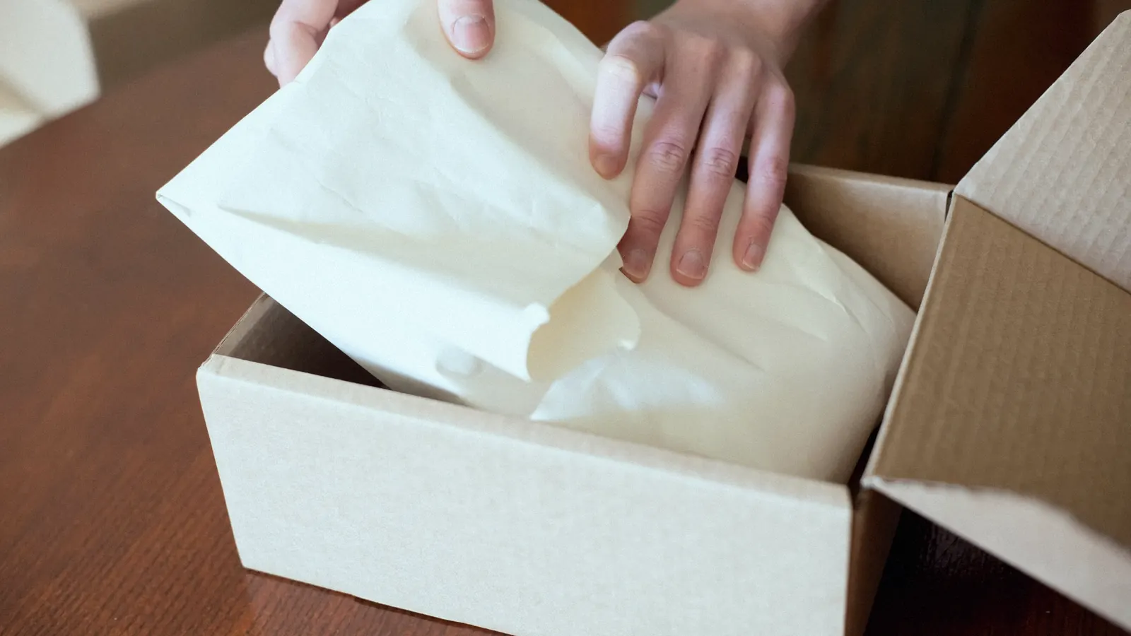 Hands packing an order into a cardboard box.